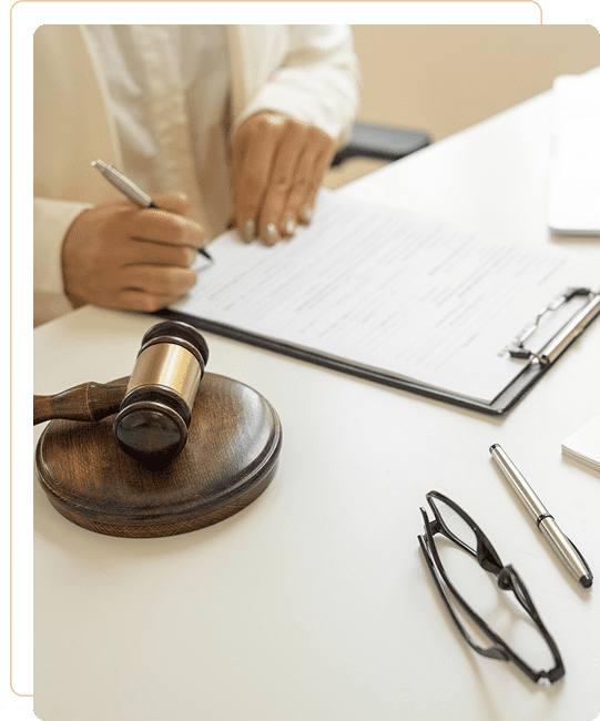 Legal professional signing documents with a gavel and glasses nearby.